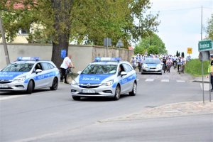 Radiowóz a za nim uczestnicy rajdu przejeżdżają przez skrzyżowanie, które jest blokowane przez policjanta.