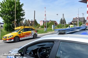 Pojazdy z umieszczonymi na bagażnikach rowerami mijają stojący na poboczu radiowóz.